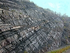 Pound Gap where most of this photograph is of the middle portion of the Mississippian Grainger Formation. Here this is composed of alternating relatively continuous to occasionally shallowly channeled beds of sand with uniform sharp bedding planes and shale; both lithologies vary in thickness and the sands often exhibit Bouma sequences suggesting deposition from turbidite currents that were active over a mid to outer fan setting