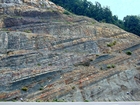 The base of the visible portion this road cut marks the top the Lower Mississippian Sunbury Shale that is locally coffee colored. Most of the photograph is of the Mississippian Grainger Formation which is composed of alternating relatively continuous to occasionally shallowly channeled beds of sand with uniform sharp bedding planes and shale; both lithologies vary in thickness and the sands often exhibit Bouma sequences suggesting deposition from turbidite currents that were active over a mid to outer fan setting. The lower portion of the formation is shale rich and probably from a deeper water setting and a more distal portion of the fan. At the top of the photograph is the overlying Lower Mississippian Newman Limestone Formation