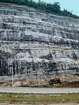 At the base of the photograph is a small exposure of the Mississippian Grainger Formation with continuous beds of sand with uniform sharp bedding planes and shale. Most the upper portion of the photograph is the Lower Mississippian Newman Limestone Formation. This is composed of relatively continuous beds of shallow water carbonate that locally develop mounds and are channeled. Beds have irregular but sharp bedding planes, some shale partings and dolomitic siltstones