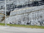 At bottom right brown round surface marks top of unit 111 and base of 110, see the measured Geological Section, Kentucky Geological Survey Field Trip Guide 1998. Tan layer marks top of 110 and base of 109. Photograph of the Lower Mississippian Newman Limestone Formation. Here relatively continuous beds of shallow water carbonate that locally develop mounds and are channeled. Beds have irregular but sharp bedding planes. Note the dolomitized siltstone layers scattered through the outcrop that form clear markers