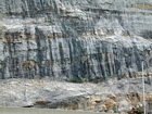 Storm waves are interpreted to have eroded this shelf surface and caused the shallow water limestones of the Lower Mississippian Newman Limestone Formation to have their irregular character, while local currents account for the development of low angle cross beds and mound margin clinoforms suggesting migrating carbonate bodies moving across this setting. Note two prominent beds of dolomitized silt interbedded with the shallow carbonates in the center of this image. These are interpreted to be the product of subaerial exposure and windblown transport to their current, probably marine depositional setting. Close to the center of the photograph are irregular brecciated dolomites associated with subaerial exposure. Base is unit 114 with 112 between tan layers, see the measured Geological Section, Kentucky Geological Survey Field Trip Guide 1998. 