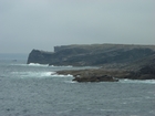 Cliffs and eroded bedding planes of the coastal monocline of Namurian deepwater sediments of the Ross Formation, overlain by turf covered Pleistocene drift. Fisherman's Point ledge is situated in the middle background to the north. In foreground are bedded and slumped sediments of the Ross Formation.