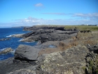 Eroded bedding planes of the coastal monocline of Namurian deepwater sediments of the Ross Formation, overlain by turf covered Pleistocene drift. Fisherman's Point ledge can be seen in the middle background to the north.