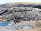 Cliffs and eroded bedding planes of the coastal monocline of Namurian deepwater sediments of the Ross Formation just south of Fisherman's Point. In foreground are bedded and slumped sediments of the Ross Formation.