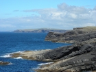 Cliffs and eroded bedding planes of the coastal monocline of Namurian deepwater sediments of the Ross Formation, overlain by turf covered Pleistocene drift. Fisherman's Point ledge is situated in the middle background to the north. In foreground are bedded and slumped sediments of the Ross Formation.