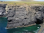 The Ross Formation of Loop Head is here expressed as turbidite sheet sands that accumulated as deepwater fan lobes that were dissected by sparse shallowly incised channels. As Elliot (2000) records these are the thicker bedded, high net-to-gross, sheet turbidites of the lower part of the Ross Sandstone Formation turbidite system. The height of these cliffs is between 45-50 m. Note the shaley partings that may compartmentalize these sands and seperate them in terms of their reservoir quality from those above. Shallow though the channeling may be it may enhance vertical reservoir continuity between the stacked sheets