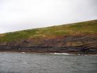 West end of Rehy Cliffs just east of a monocline. At level of sea and above are mixed thin bedded inter channel sands. Above is an amalgamated channel fill with feather edge of channel wings. Downlapping onto this channel sand are clinoforms interpreted to be filling the eroded interior of a channel.