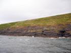 West end of Rehy Cliffs just east of a monocline. At level of sea and above are mixed thin bedded inter channel sands. Above is an amalgamated channel fill with feather edge of channel wings. Downlapping onto this channel sand are clinoforms interpreted to be filling the eroded interior of a channel.