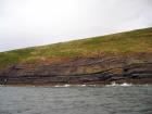 West end of Rehy Cliffs just east of a monocline. At level of sea and above are mixed thin bedded inter channel sands. Above is an amalgamated channel fill with feather edge of channel wings. Downlapping onto this channel sand are clinoforms interpreted to be filling the eroded interior of a channel.