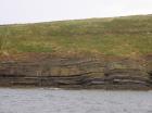 West end of Rehy Cliffs just east of a monocline. At level of sea and above are mixed thin bedded inter channel sands. Above is an amalgamated channel fill with feather edge of channel wings. Downlapping onto this channel sand are clinoforms interpreted to be filling the eroded interior of a channel.