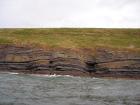 West end of Rehy Cliffs just east of a monocline. At level of sea and above are mixed thin bedded inter channel sands. Above is an amalgamated channel fill with feather edge of channel wings. Downlapping onto this channel sand are clinoforms interpreted to be filling the eroded interior of a channel.