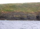 West end of Rehy Cliffs just east of a monocline. At level of sea and above are mixed thin bedded inter channel sands. Above is an amalgamated channel fill with feather edge of channel wings. Downlapping onto this channel sand are clinoforms interpreted to be filling the eroded interior of a channel.