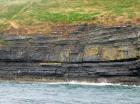 West end of Rehy Cliffs just east of a monocline. At level of sea and above are mixed thin bedded inter channel sands. Above is an amalgamated channel fill with feather edge of channel wings. Downlapping onto this channel sand are clinoforms interpreted to be filling the eroded interior of a channel.