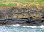 West end of Rehy Cliffs just east of a monocline. At level of sea and above are mixed thin bedded inter channel sands. Above is an amalgamated channel fill with feather edge of channel wings. Downlapping onto this channel sand are clinoforms interpreted to be filling the eroded interior of a channel.