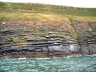 Rehy Cliffs thin bedded interfingering inter channel sands overlying a sandstone body representing an amalgamated deepwater channel fill just above the present sea level, highlighted by gull droppings. Ross Sandstone Formation probably in mid fan position towards center of fan body.