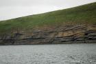 West end of Rehy Cliffs just east of a monocline. At level of sea and above are mixed thin bedded inter channel sands. Above is an amalgamated channel fill with feather edge of channel wings. Downlapping onto this channel sand are clinoforms interpreted to be filling the eroded interior of a channel.